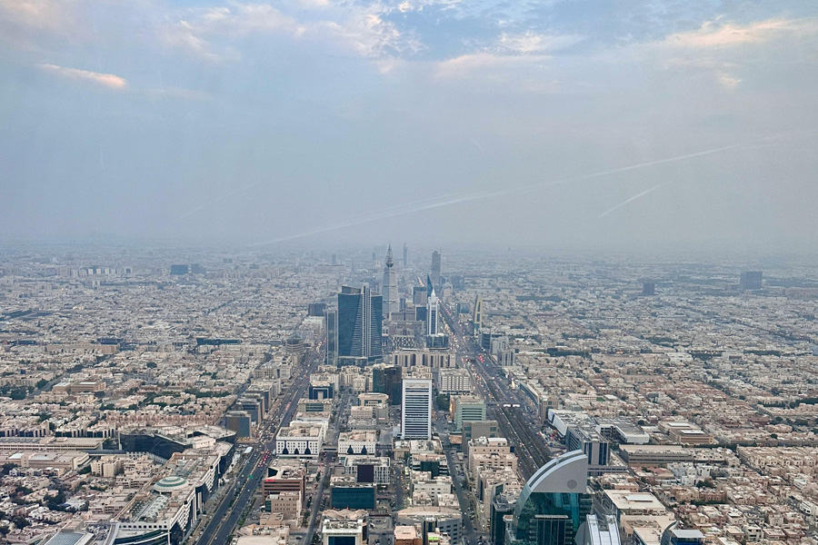 Aerial view of Riyadh cityscape with skyscrapers and urban sprawl under a cloudy sky.